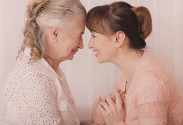Home Care Assistance - San Antonio caregiver holding the hands of senior woman and touching foreheads